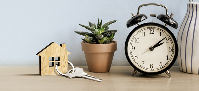 Model House with key on the table with alarm clock near blue wall background