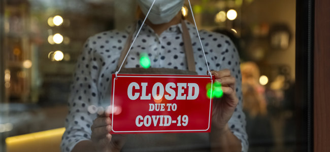 Woman in mask putting red sign with words Closed Due To Covid-19